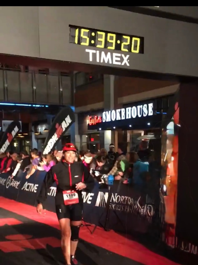 Trish crossing an Ironman finish line beneath the race clock